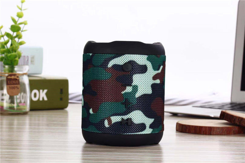 Camouflage-patterned speaker on a desk with a laptop and plant in the background